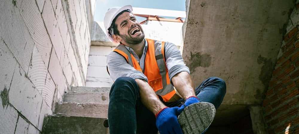 Workers' Comp Claim Denied in Illinois? What to Do Next 1 A construction worker in a hard hat and safety vest holding his injured foot on a job site staircase