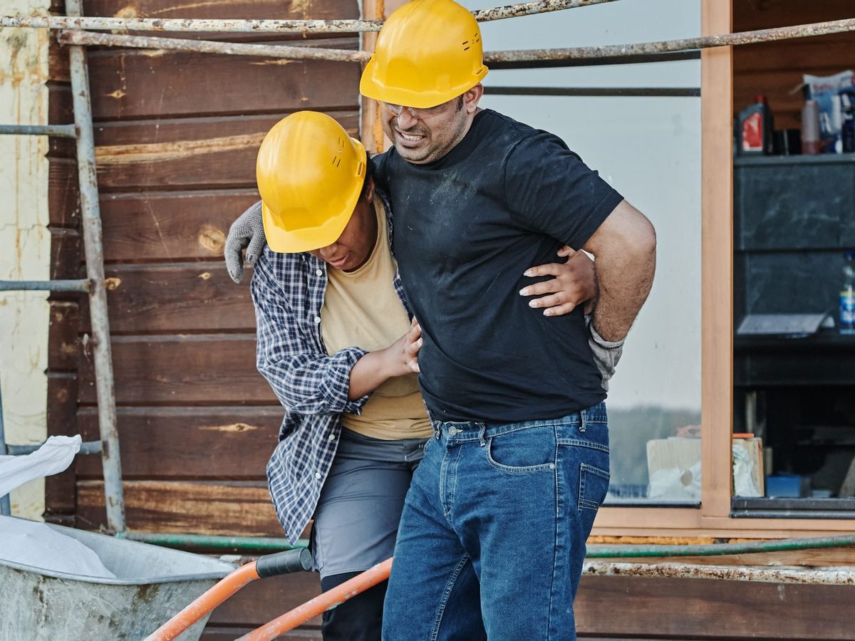 Illinois Workers' Comp IME: What to Expect at the Employer's Medical Exam 1 Construction worker holding his lower back in pain while a coworker supports him at a job site